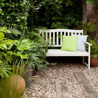 Wooden garden bench on stone path surrounded by plants