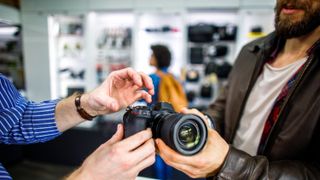 Store clerk explaining the functions of a DSLR camera to an interested shopper in a camera shop.