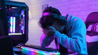 Upset PC gamer with head in hands by their PC