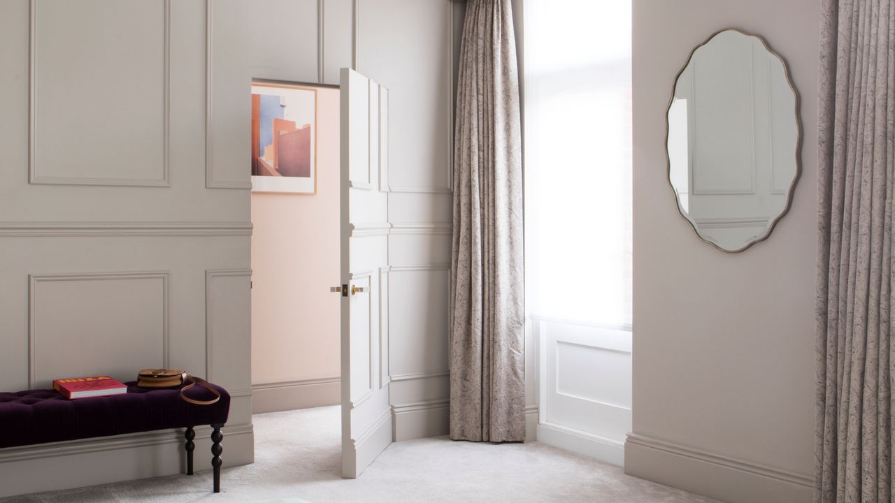 Mirror hanging on wall in light coloured bedroom with wall panelling