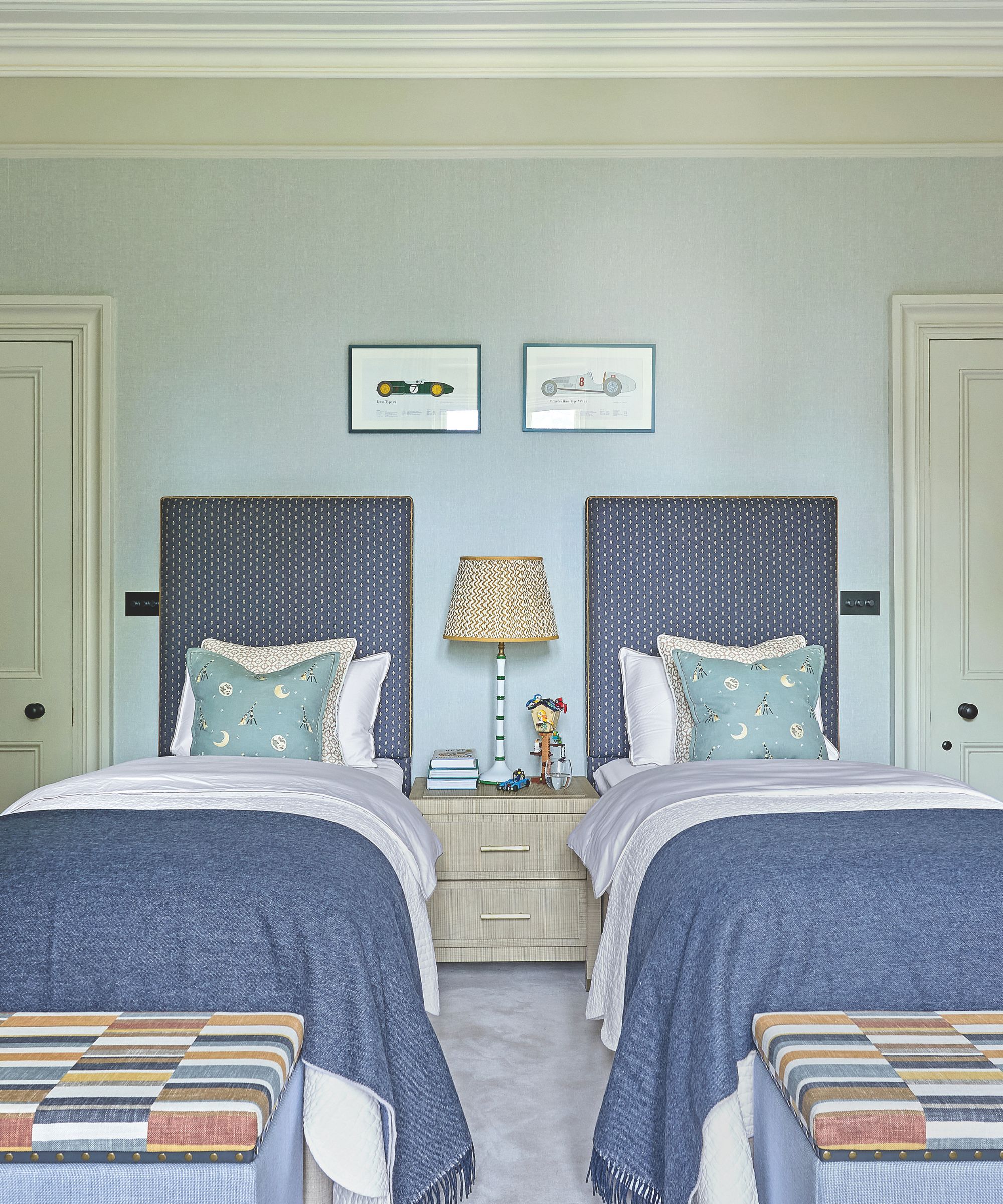 Pale blue twin bedroom with large blue headboards and blue blankets at the end of each bed