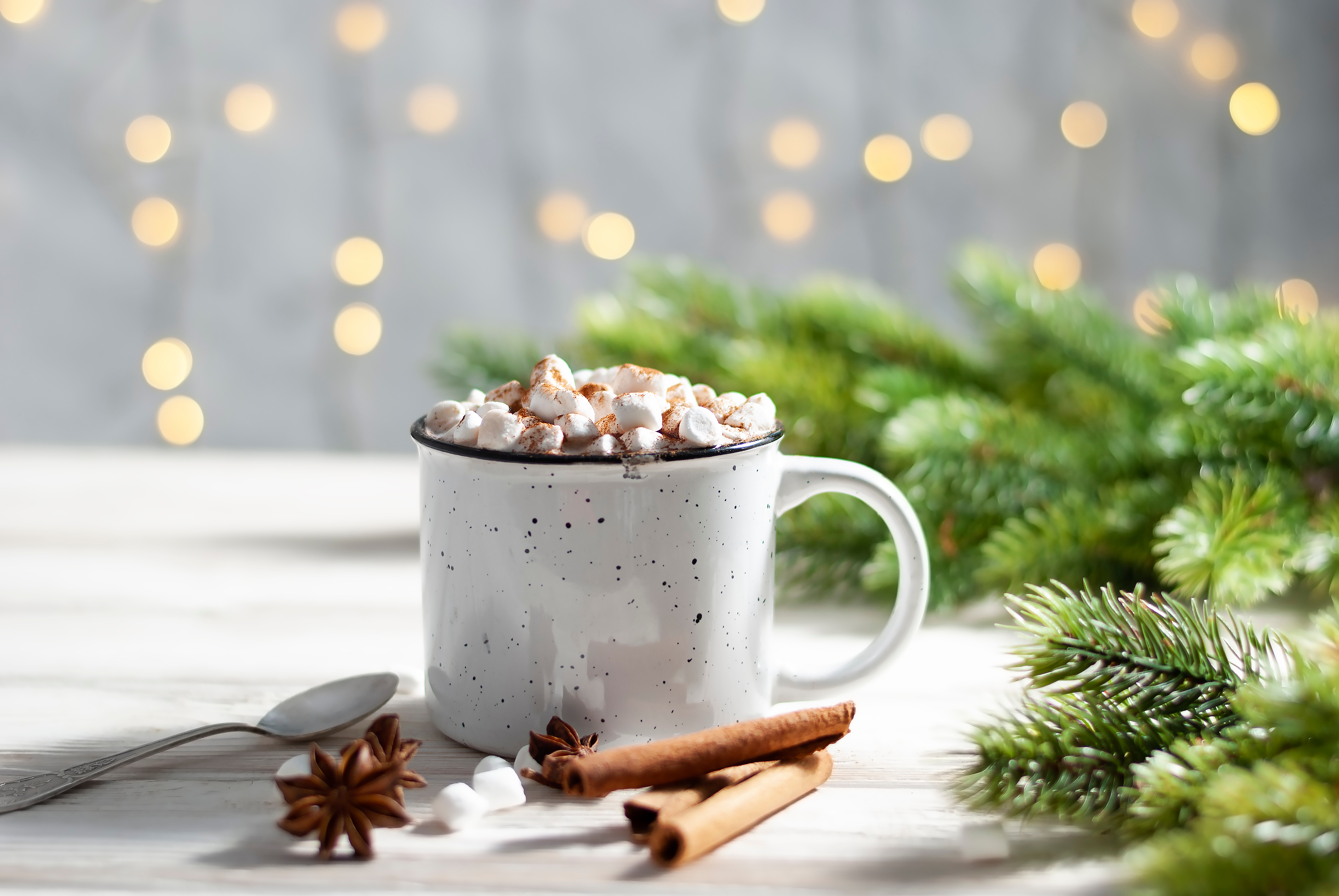 a christmas drink with marshmallows and cinnamon and cloves in a white mug with a christmas tree in the background