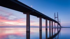 A bridge spans a large body of water at sunset.