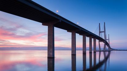 A bridge spans a large body of water at sunset.