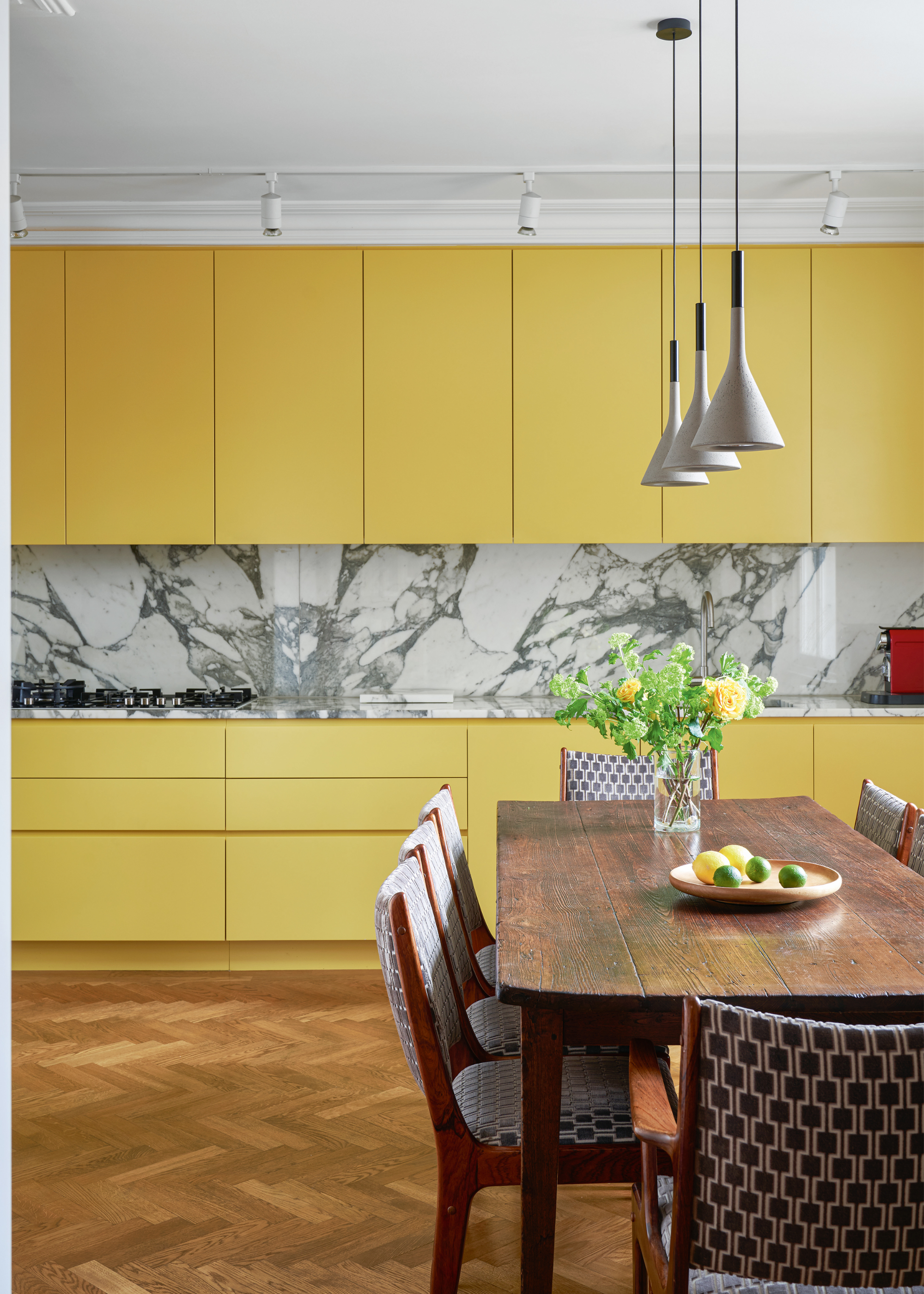 Yellow kitchen with marble splashback and a vintage wooden dining table in front