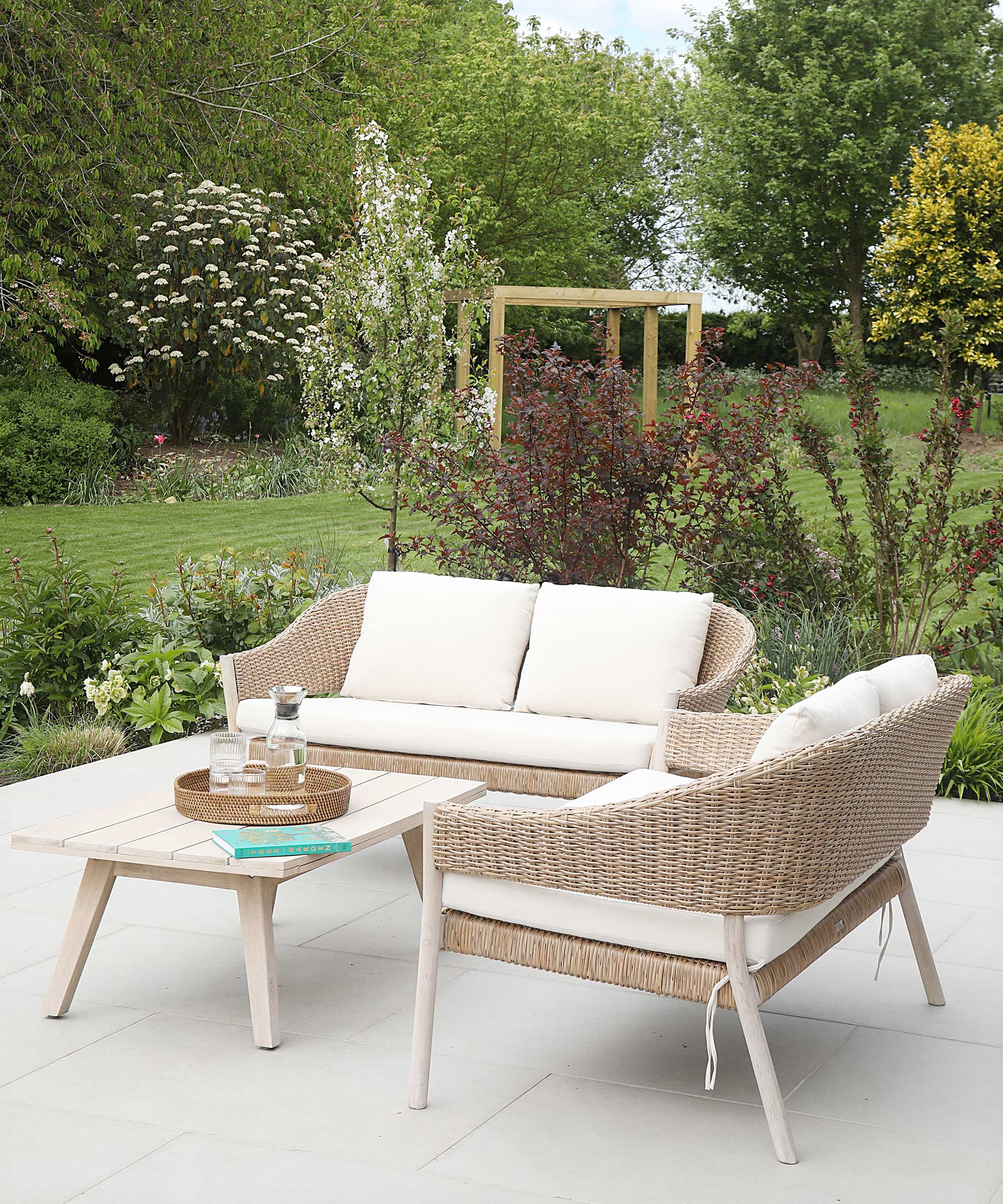 small modern patio with pale coloured paving, rattan sofas with white cushions and a small coffee table