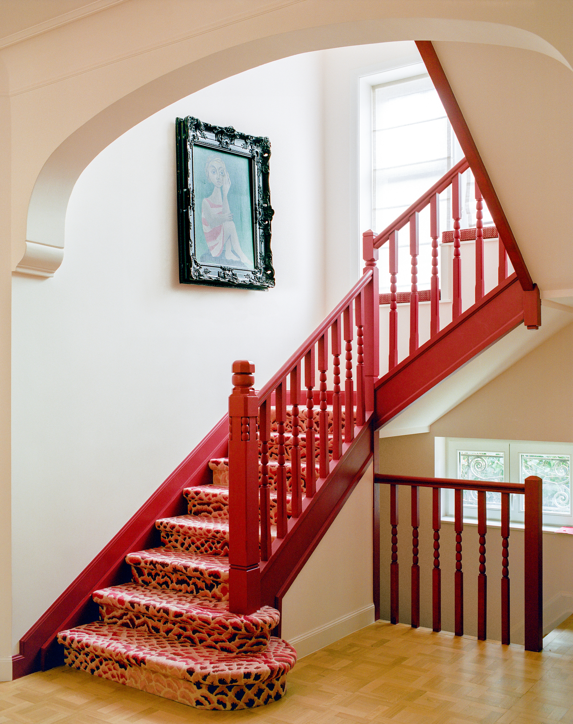 Image of a bright red staircase with a red patterned runner in a white stairwell.