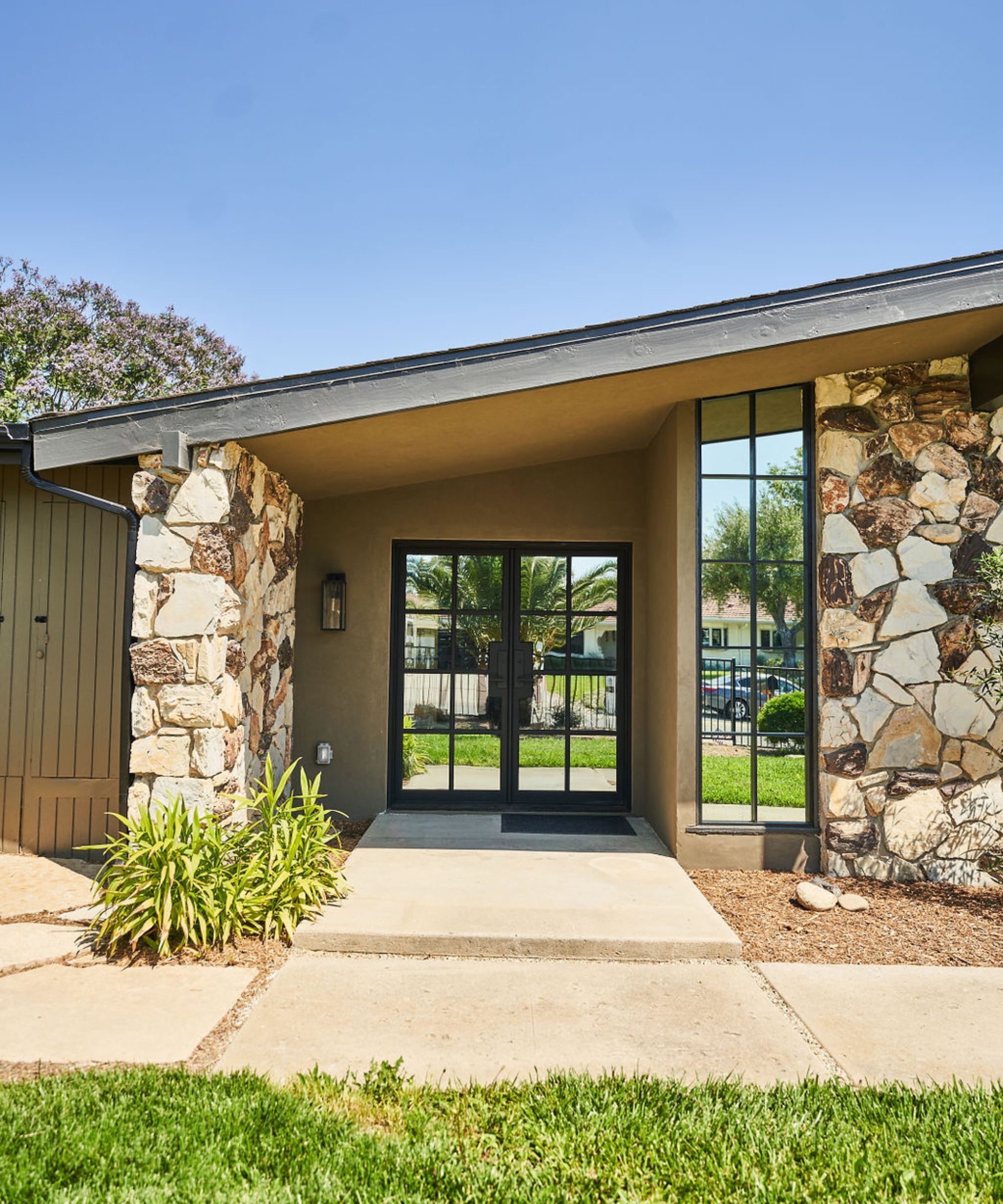 A modern bungalow with a sloped roof, exposed brickwork on each side of the black and mirrored front door, a paved path, and a grass lawn.