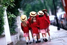 Group of schoolgirls aged 5-7 walk down the street wearing school uniform and straw boater hats.