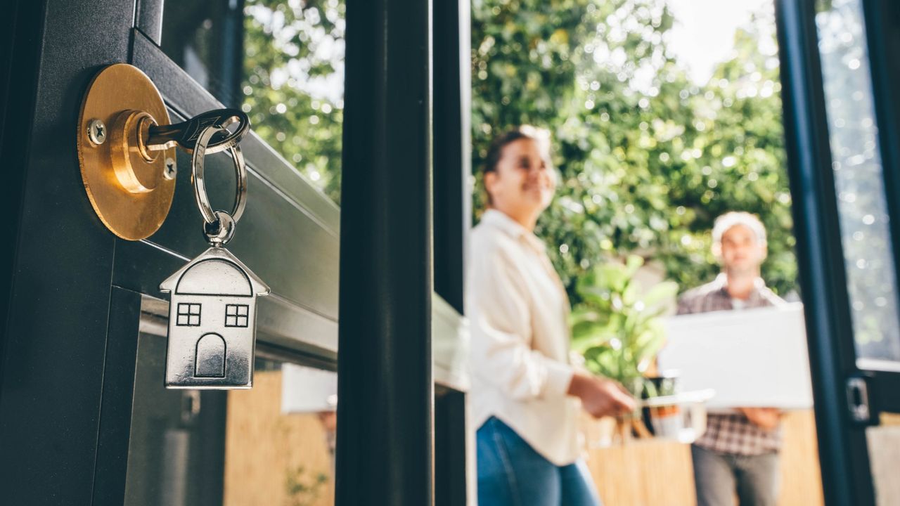 Key in door with homemovers in background