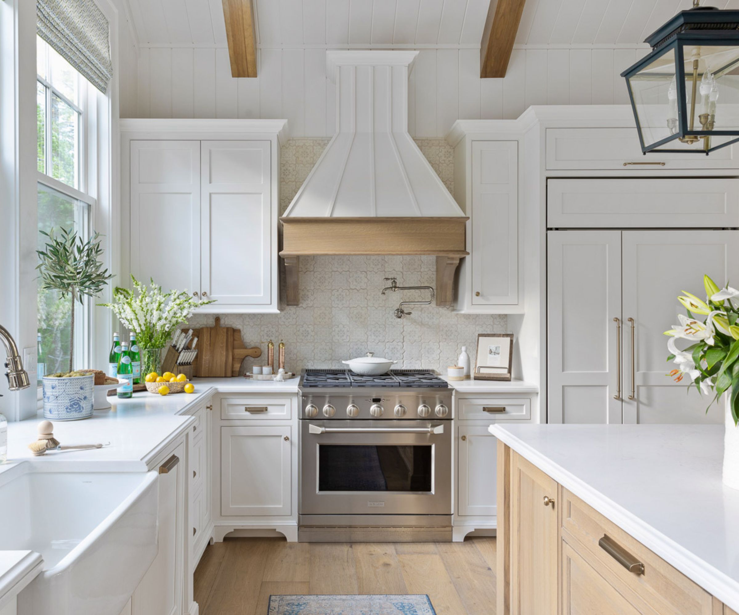 A white kitchen with shaker cabinets, exposed wooden beams, and paneling on the upper walls and ceiling