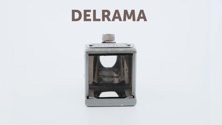 A small cube-shaped lens adapter for a camera. It has a glass front panel and a silver exterior. 