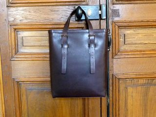 Luxury leather luggage from Mismo, Denmark. A deep dark leather bag hanging on the door nob of a wooden door.