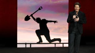 Tom Cruise in a black suit standing in front of a picture of his Digger character at CinemaCon 2026. 