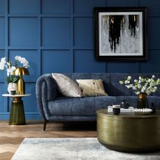 Blue sofa in a living room with a blue panelled wall and wooden herringbone floor