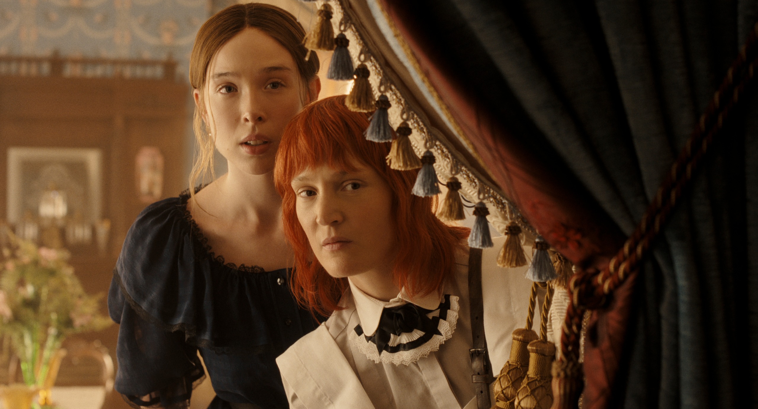 ella beatty as lizzie borden wearing a black dress and vicky krieps as bridget sullivan in a maid's uniform as they peer around a corner in a victorian era home in monster the lizzie borden story