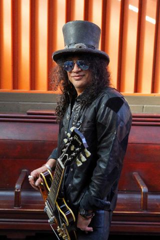 Slash in top hat and shades, holding a Gibson semi-acoustic guitar