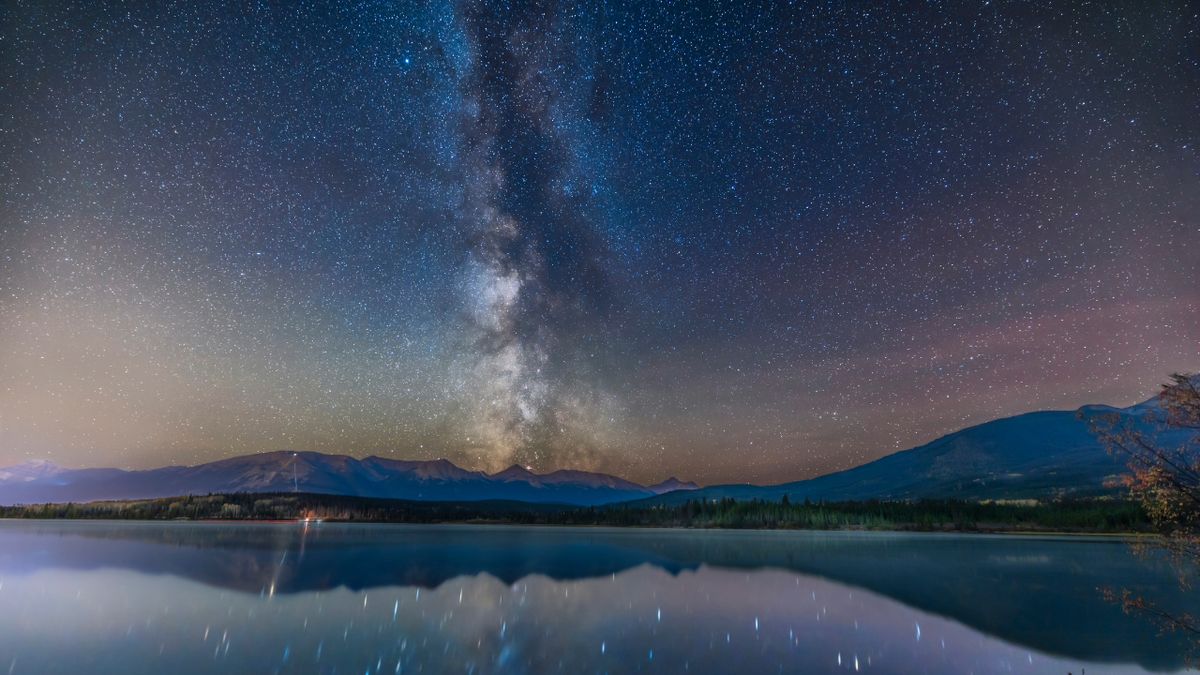 銀河系在湖上方可以看到,它仍然反映了夜空中星空的藍色和白光,紫色和藍色,遠處有一些山脈。