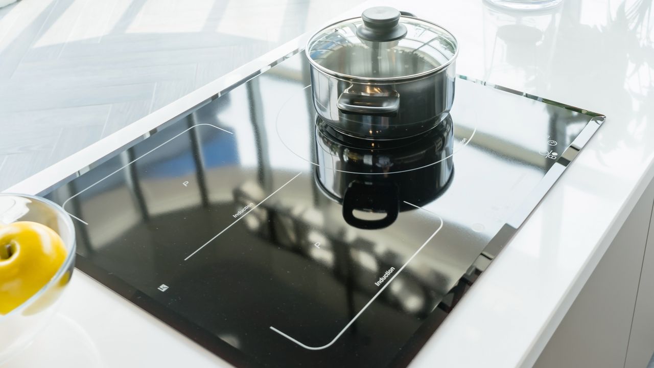 Gleaming electric stove top with pan, shot from above, and bowl of lemons to the side to illustrate how to clean an electric stove top