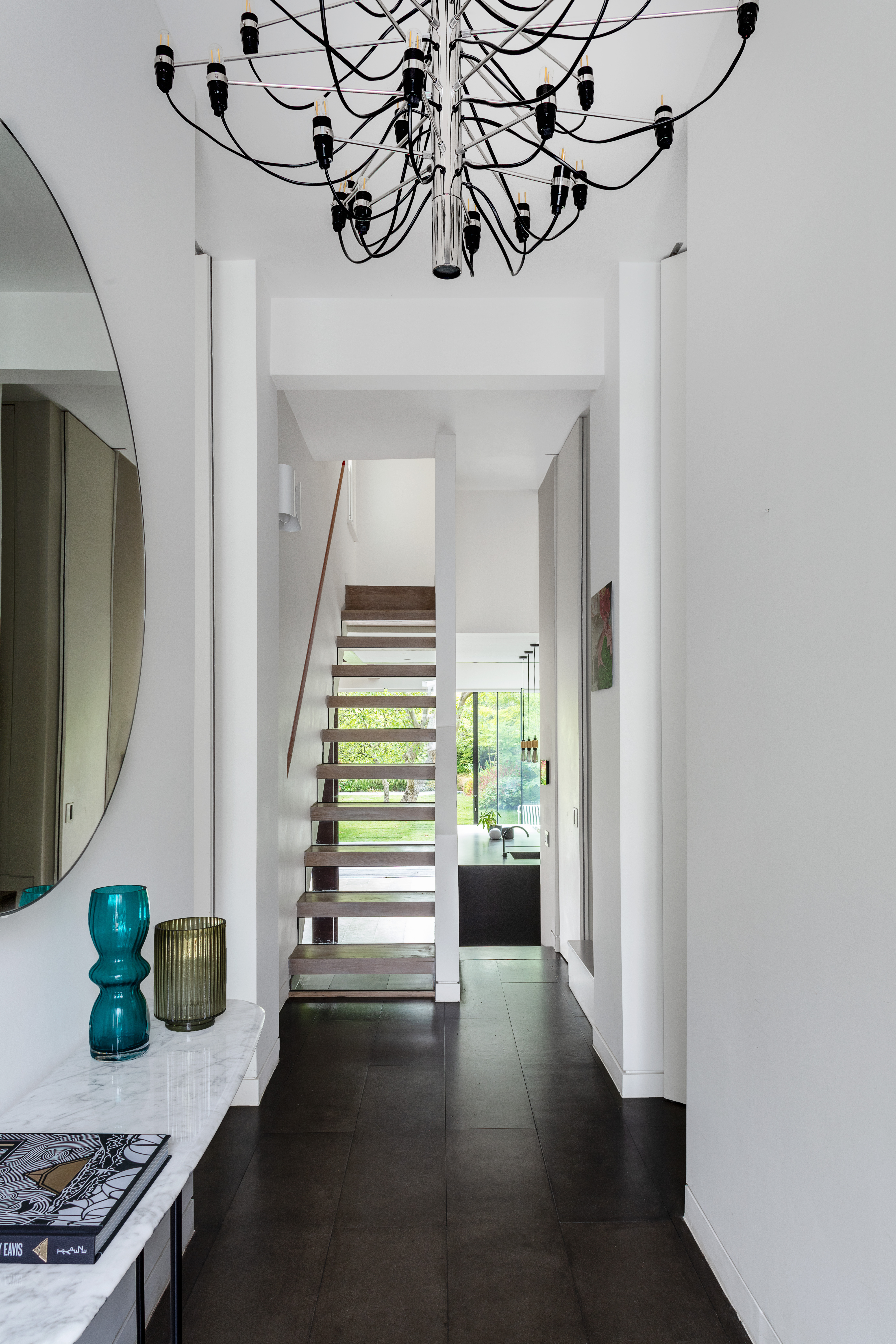 A hallway with a chandelier on the ceiling, wooden flooring, and white walls