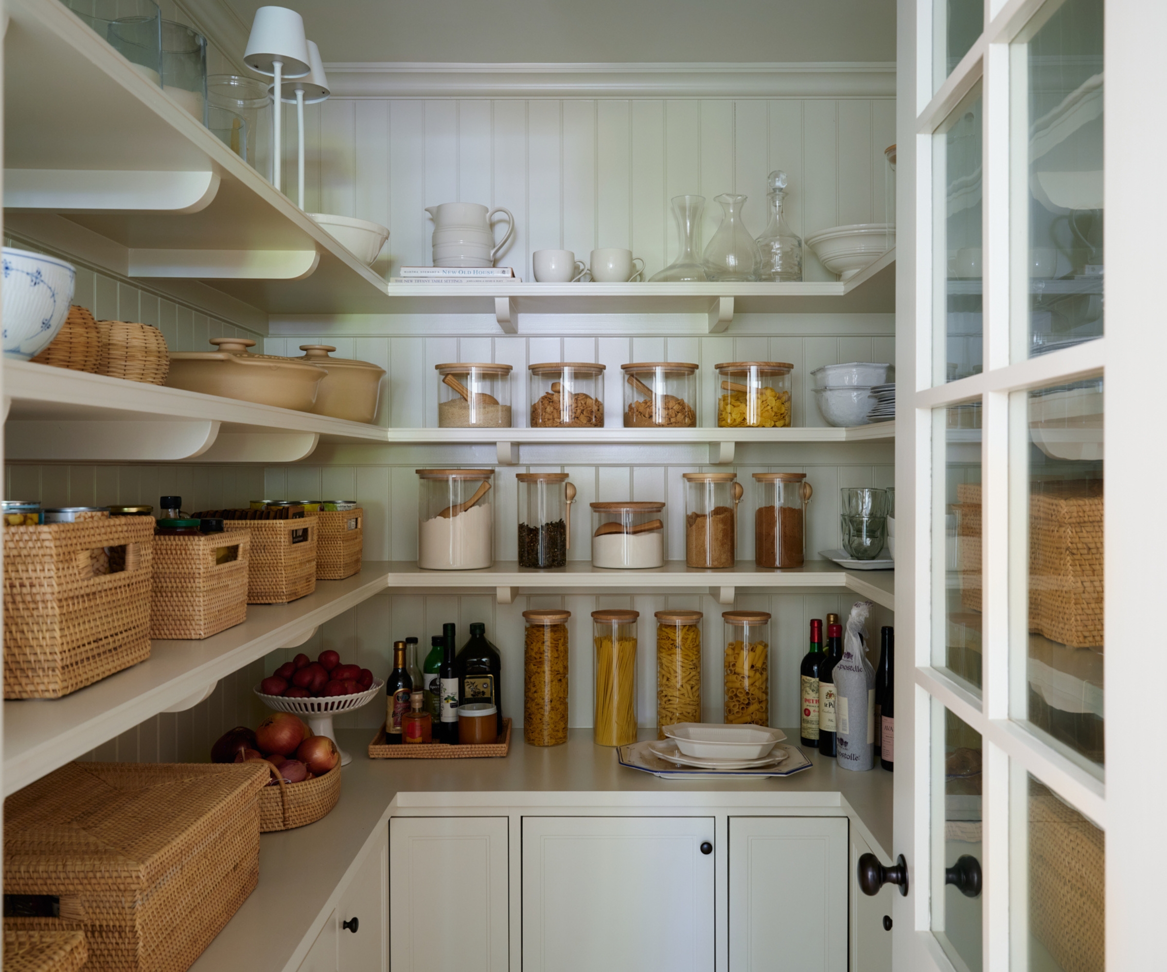 A warm white pantry with shelves filled with wood and glass canisters
