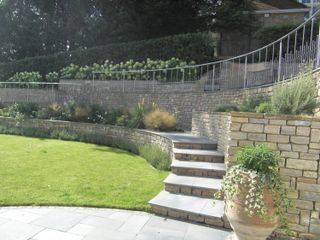sloping garden ideas: stone retaining wall and railings on the top level