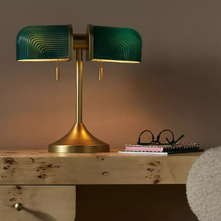 Green lamp with gold stand on a wooden desk