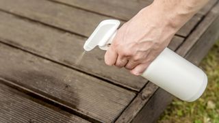 Person hand spraying insect repellent on home terrace wood boards