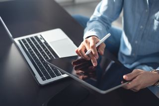 Young casual business woman sitting on the floor using stylus pen and digital tablet, working on laptop computer at home office.