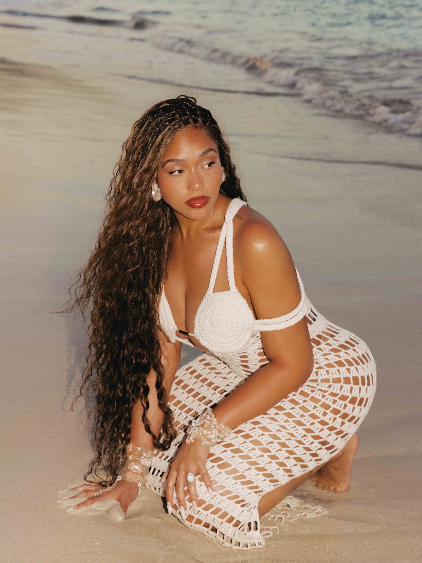 Jordyn Woods wearing a white crochet dress on the beach.