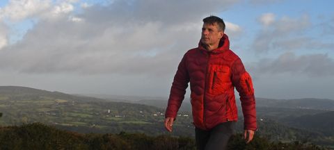 Hiker wearing a Peak Performance Helium Utility Flo Jacket on hillside above town