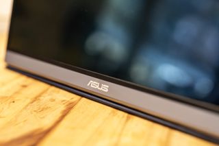 A black and silver ASUS ZenScreen MQ16AH portable monitor on a wooden brown desk