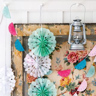 Pastel paper party decorations strung over a vintage floral picture with steel lantern