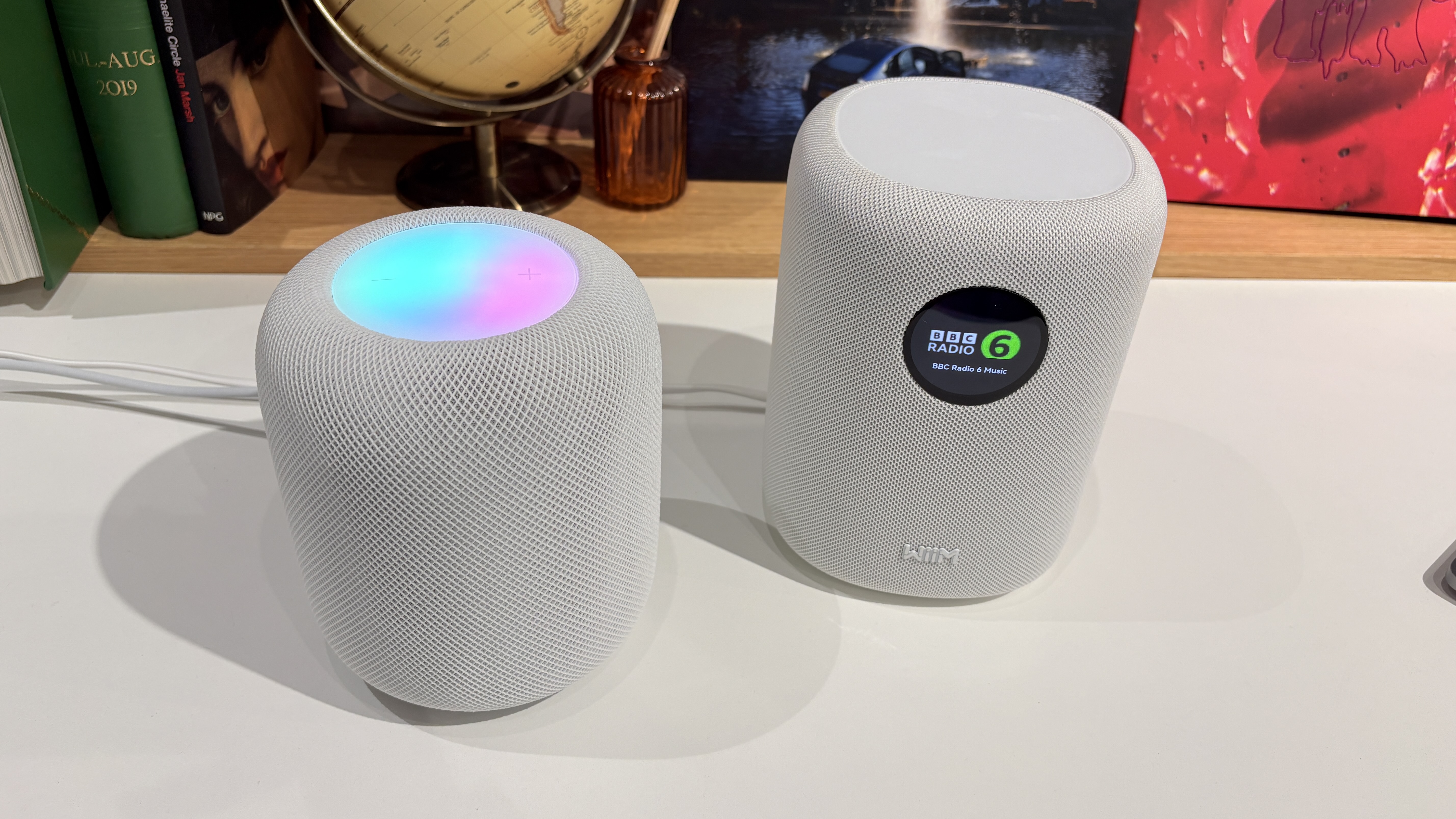 A white Apple HomePod 2 next to a white WiiM Sound on a white surface