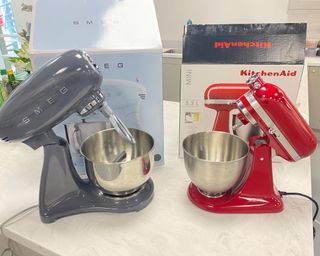 Image of KitchenAid and Smeg stand mixers in head to head image on marble countertop