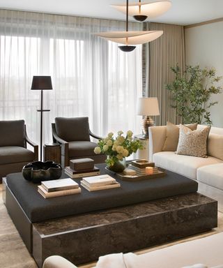 neutral contemporary living room with a large central coffee table decorated with books and flowers with two dark armchairs facing the room