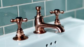 Three piece brass taps attached to white sink with high gloss teal tile behind