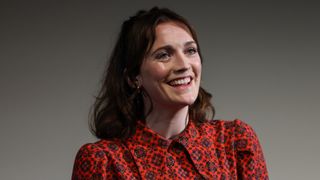  Charlotte Ritchie at a press call wearing a red dress with her brown hair shoulder length 