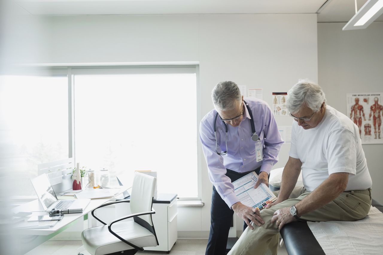 Doctor examining senior man۪s knee in examination room