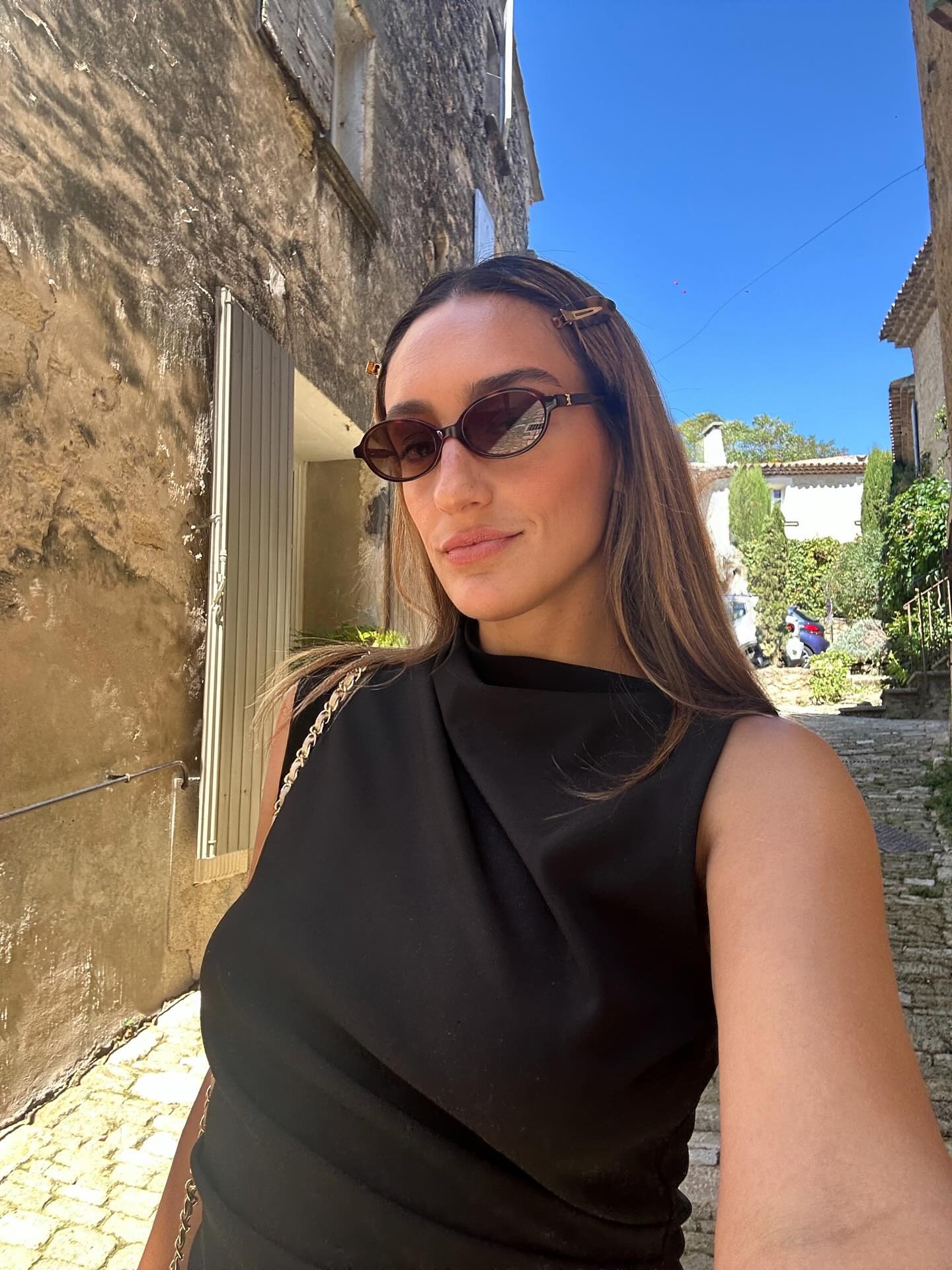 A woman taking a selfie in the sun with brunette hair and honey blonde highlights