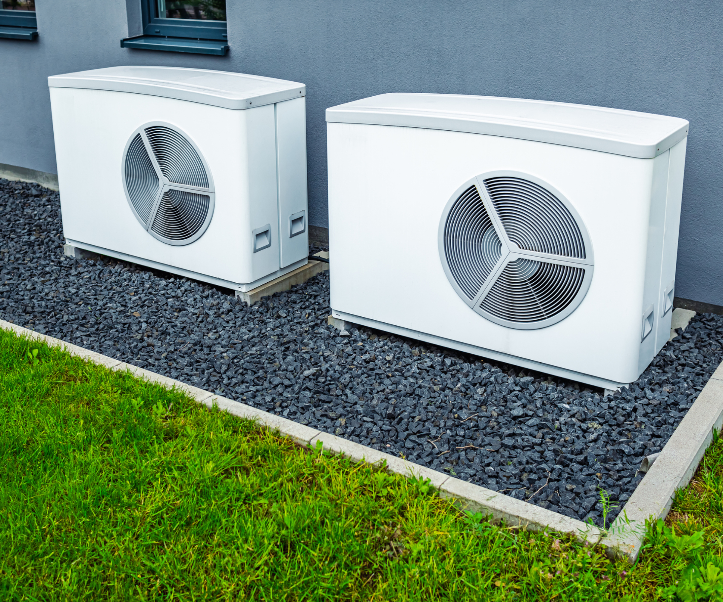 two heat pumps installed on floor outside house