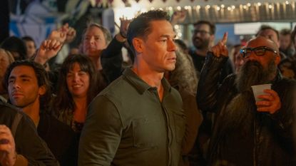 John Cena as Peacemaker in the Peacemaker season 2 finale, surrounded by a crowd of people.