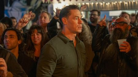 John Cena as Peacemaker in the Peacemaker season 2 finale, surrounded by a crowd of people.