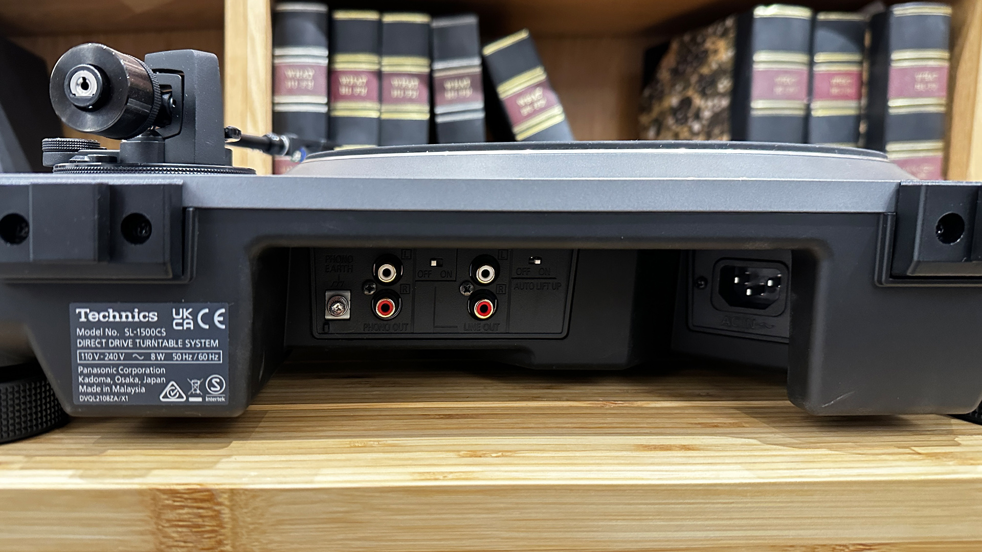 Technics SL-1500CS turntable on wooden hi-fi rack in front of bookcase, rear of turntable showing connections
