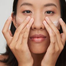 A woman applying eye cream to her face