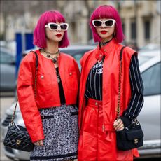 Twins Ami Amiaya & Aya Amiaya wears red cropped jacket, black white skirt, wide leg shorts, sleeveless jacket, black white striped jumper with logo outside Chanel during Paris Fashion Week - Womenswear Fall Winter 2023 2024 : Day Nine on March 07, 2023 in Paris, France.