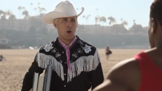 Ken standing with his mouth open on a beach. He's also holding books.