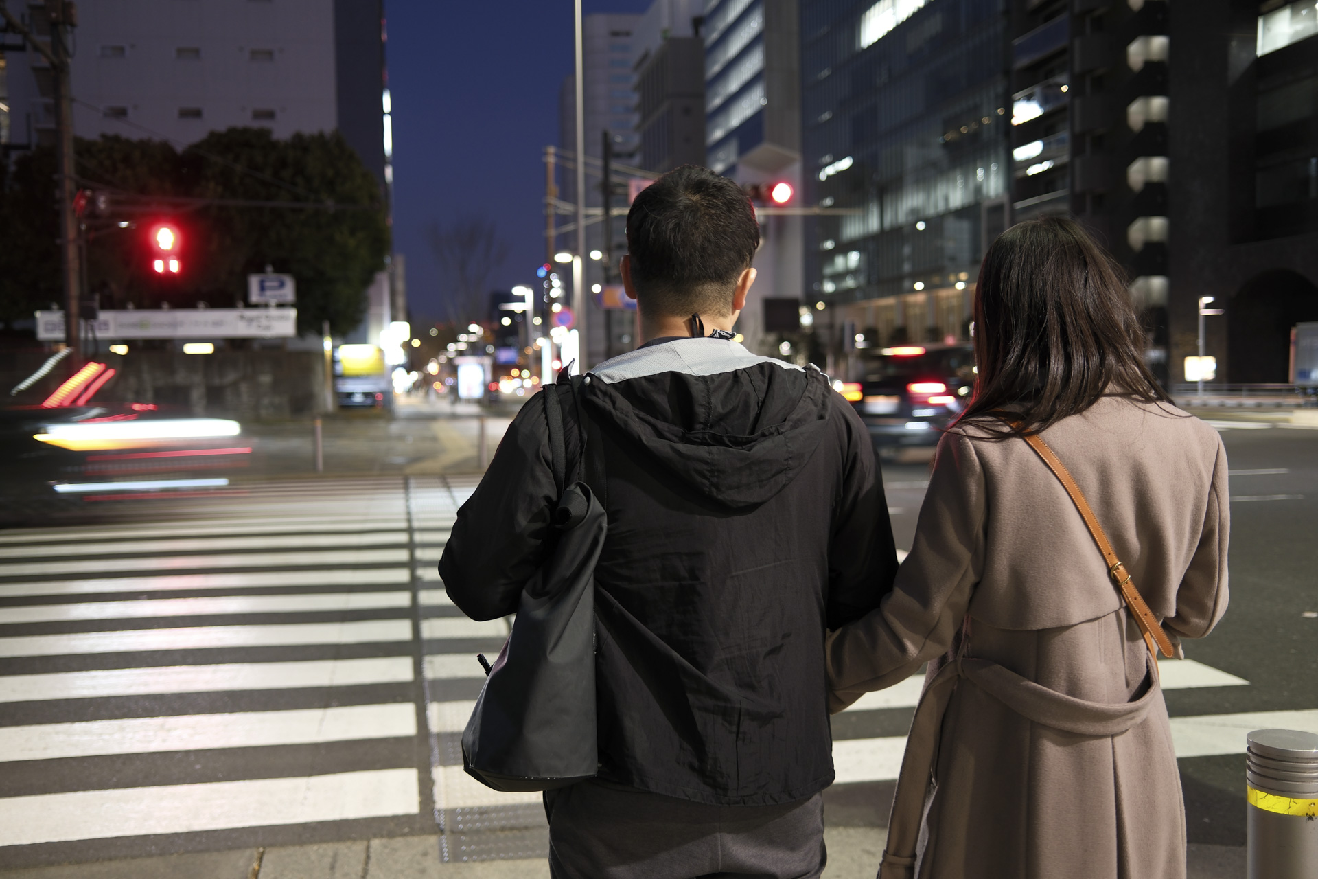 tokyo city at night, a couple waits by pedestrain crossing with light trails from moving vehicles