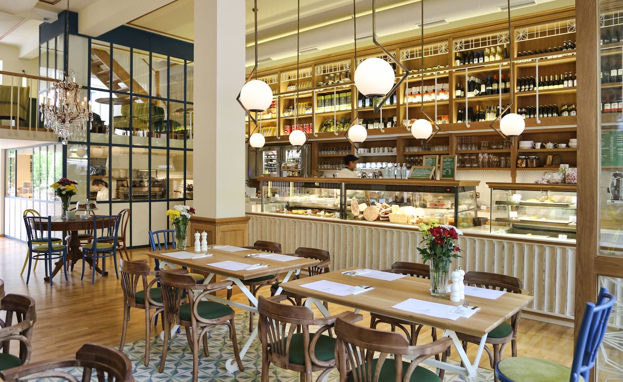 Restaurant interior with wood and glass display counter in front of wooden shelves, tiles and wooden floor and tables and chairs