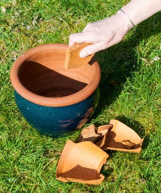 person adding pieces of a broken plant pot to the bottom of a garden planter